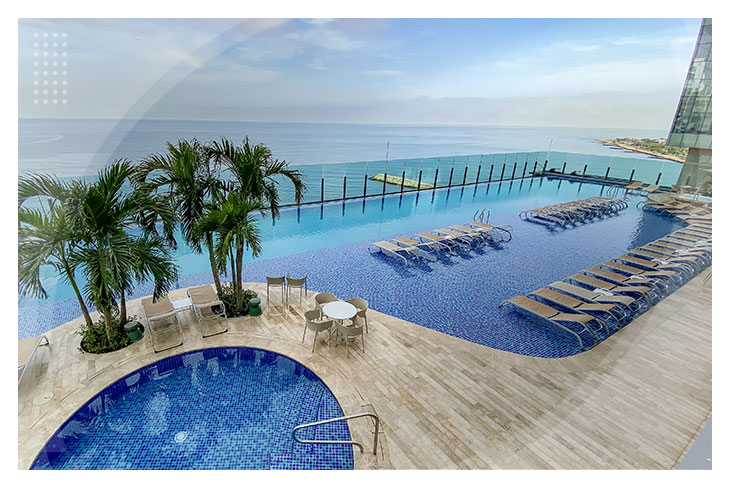 Piscina infinita con vista al mar, rodeada de palmeras, sillas asoleadorasy una zona húmeda de descanso, ideal para disfrutar en los exclusivos Hoteles Estelar de Cartagena
