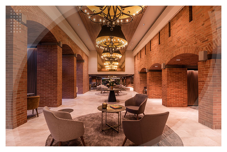 Lobby con sofás modernos, un par de mesas y decoración acogedora, rodeado de columnas y arcos de ladrillo, con grandes lámparas que iluminan este espacio en uno de los mejores hoteles de Bogotá