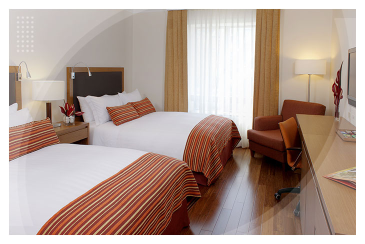 Habitación con dos camas dobles, escritorio y silla ejecutiva, disponible para reserva de habitación en el Hotel Intercontinental, con luz natural que entra por una amplia ventana con cortinas claras