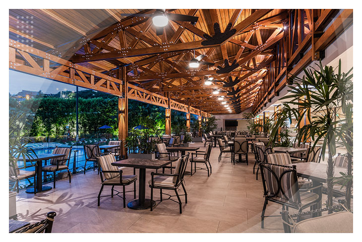 Hoteles en Cali con terraza techada en madera, mesas y sillas elegantes junto a una piscina iluminada que resalta en un ambiente acogedor