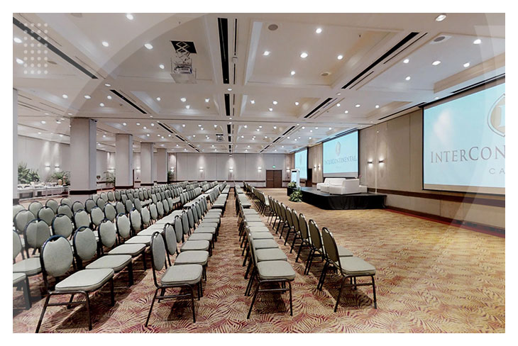 Gran salón de eventos con sillas grises y múltiples pantallas, perfecto para conferencias y reuniones en uno de los hoteles en el mejor sector de Cali
