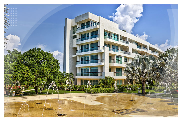 Edificio blanco de varios pisos rodeado de palmeras, jardines y fuentes de agua, en un lugar ideal para disfrutar una promoción de hoteles todo incluido en Cartagena