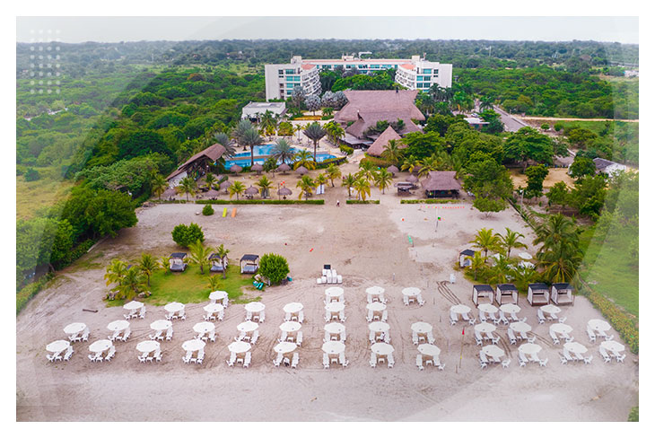 Vista aérea de una playa con sillas y sombrillas, frente al hotel rodeado de árboles y palmeras, perfecta para quienes buscan hoteles en Playa Manzanillo a bajo precio