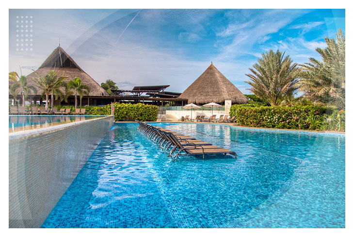 Piscina con sillas asoleadoras dentro del agua, rodeada de palmeras y construcciones con techo en palma, perfecta para quienes buscan reservas en el hotel Playa Manzanillo con descuento