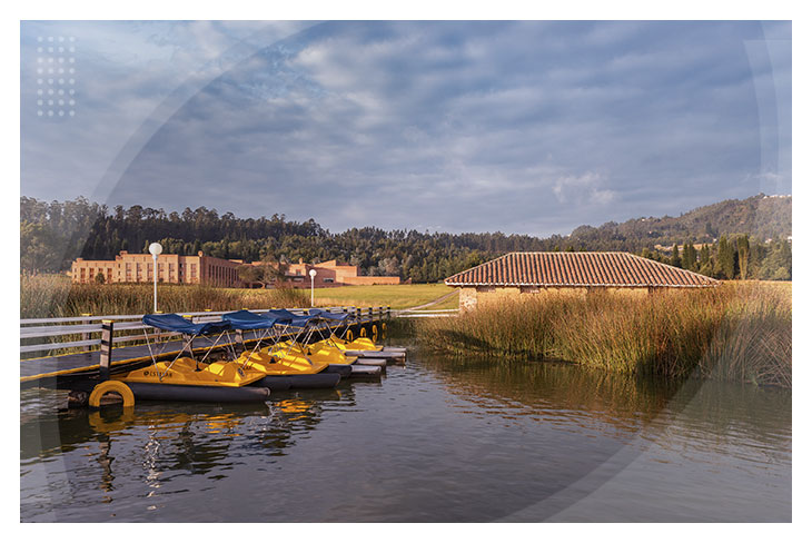 Muelle con botes de pedal amarillos rodeado de vegetación y vista al hotel de fondo y un cielo despejado, ideal para disfrutar de la promoción en hoteles Estelar para reservar en Paipa