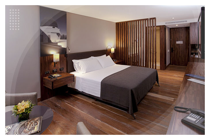 Habitación con cama doble, sábanas blancas, piso en madera y muebles de estilo moderno, en uno de los espacios diseñados para el descanso en los Hoteles Estelar de Bogotá