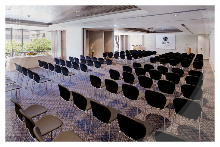 Auditorio amplio con sillas negras organizadas en filas, luz natural, pantalla de proyección, y espacios cómodos para reuniones, disponible como parte de la oferta del Hotel Estelar Parque de la 93