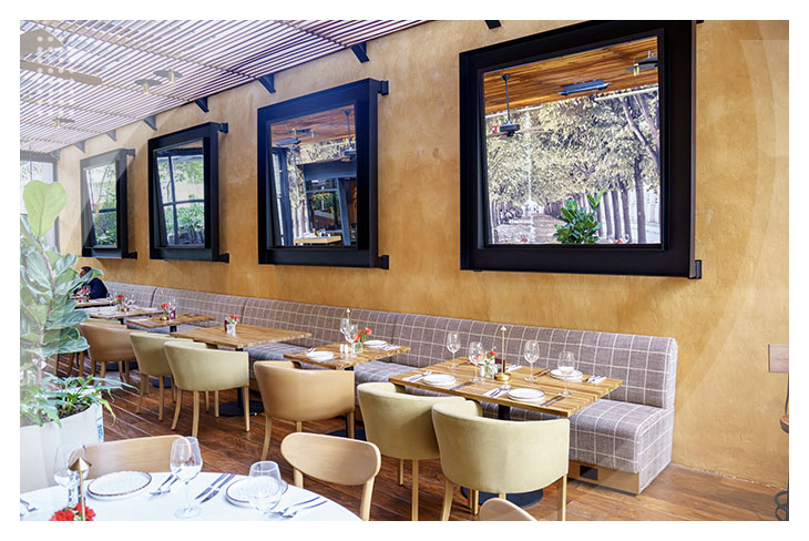 Restaurante con mesas de madera junto a una pared con ventanas amplias, sillas modernas y decoración acogedora en uno de los espacios gastronómicos que puedes disfrutar en los Hoteles con descuento de la Calle 93