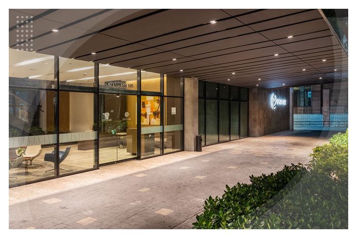 Entrada principal del hotel Estelar Square de Medellín, que cuenta con amplios ventanales, iluminación cálida y está rodeada de naturaleza