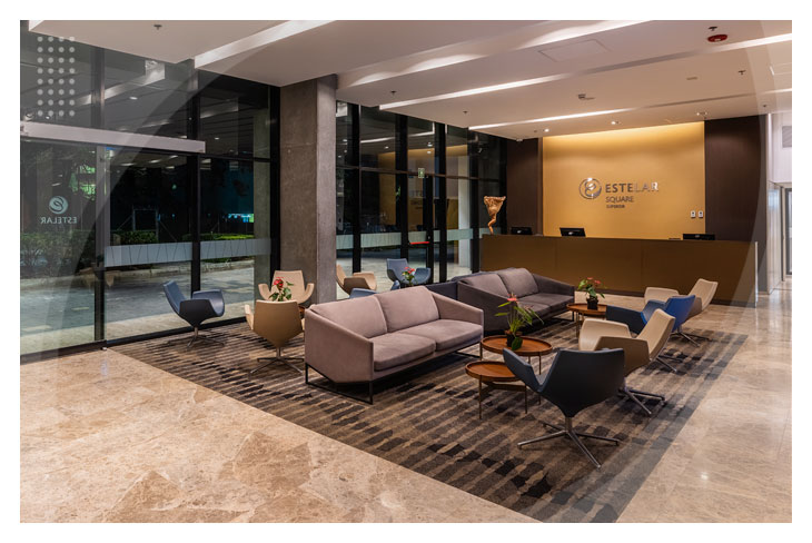 Zona de recepción en la que se pueden adquirir los descuentos en el Hotel Estelar Square El Poblado, que cuenta con sofás grises confortables y ventanales de piso a techo