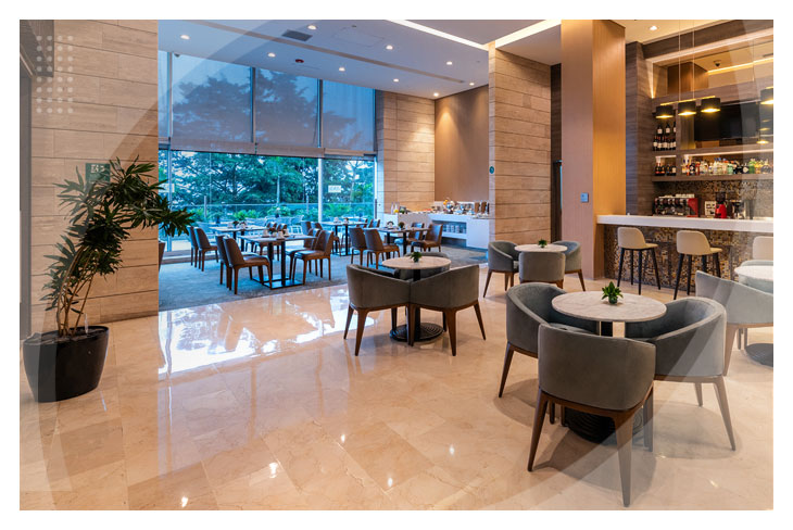 Restaurante de uno de los mejores hoteles en el Poblado Medellín, que cuenta con múltiples mesas y sillas, acompañado de un gran ventanal y una barra de bebidas