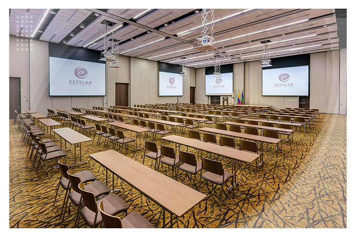 Salón de conferencias con mesas rectangulares, múltiples sillas, pantallas gigantes y sistemas de proyección, ideal para reuniones corporativas dentro de la oferta de hoteles en Villavicencio