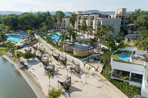 Vista panorámica del centro vacacional Lagomar, que muestra un lago, zonas verdes, piscinas, palmeras, edificios y más