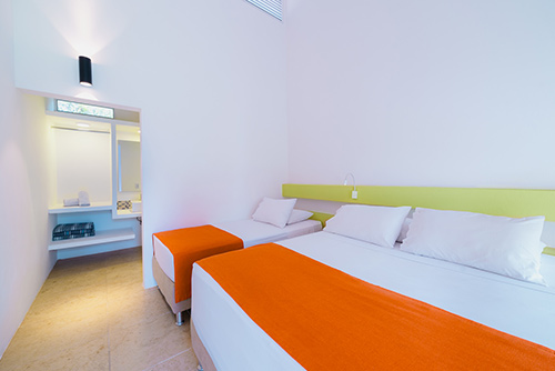 Habitación del hotel y centro vacacional Las Palmeras  en donde se encuentran dos camas, una doble y otra individual, con un corredor que va hasta el baño de paredes blancas y un amplio espejo