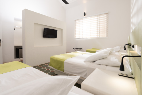 Habitación perteneciente a los descuentos especiales del centro vacacional Las Palmeras con dos camas dobles y mesas de noche para cada una, un televisor, un armario, un ventilador y una ventana