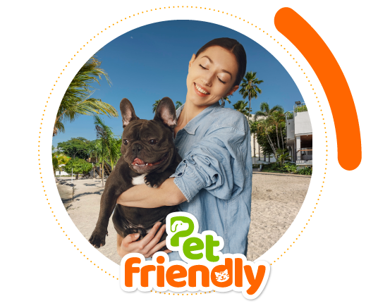 Plano cerrado de un perro de raza pequeña, de color blanco con negro, que tiene la boca abierta expresando sorpresa y se encuentra en un hotel con playa; en la parte inferior de la imagen hay un letrero de color verde y naranja con la frase pet friendly