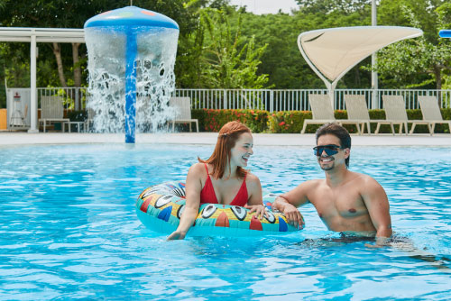 Pareja que está dentro de una piscina de agua cristalina se apoya en un flotador circular, en una de las áreas recreativas a las que accedieron al adquirir uno de los planes vacacionales en Lagosol