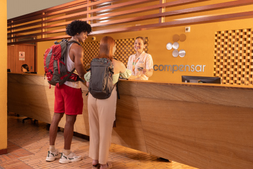 Pareja, que está frente a una recepción con muebles de madera, hace su registro con la persona encargada para acceder a las mejores tarifas y planes del hotel Lagosol Compensar