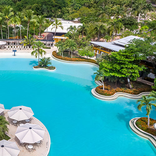 Fotografía panorámica que muestra una piscina y un conjunto de mesas playeras que hace parte de las instalaciones en donde se desarrollan los distintos planes de fin de semana del Hotel Lagosol