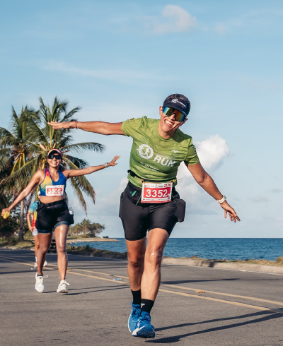 Mujer, vestida con prendas de color verde y negro, extendiendo sus brazos y celebrando haber terminado la maratón del plan turístico vuelta atlética San Andrés