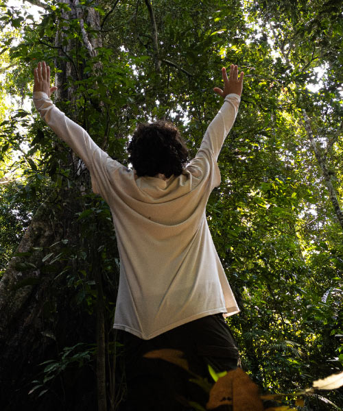 Persona con camisa blanca levantando los brazos mientras camina por un sendero rodeado de vegetación en la selva amazónica
